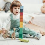 Adorable child playing with colorful wooden blocks and toy animals indoors.