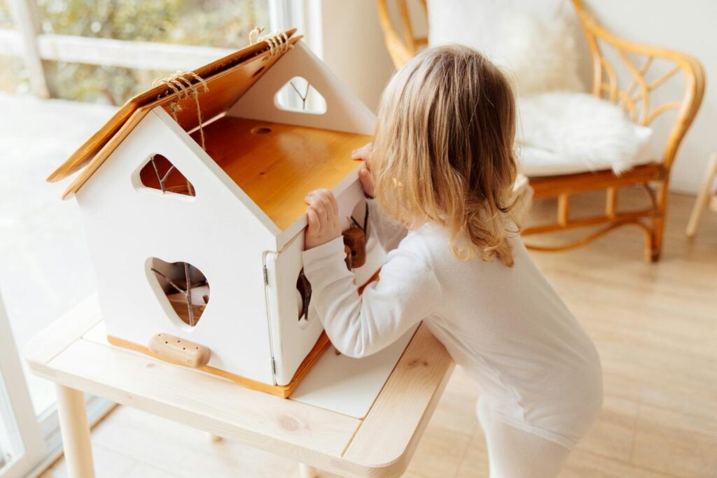 A young child engaging with a wooden dollhouse in a sunny, cozy playroom.