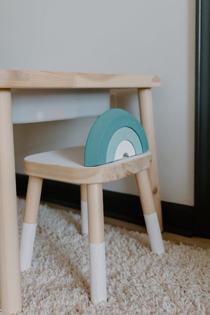 Wooden children's chair with blue accent beside a matching table on a carpeted floor.