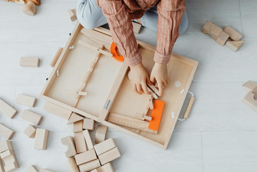 A child playing with wooden blocks and a toy set on a light floor, fostering creativity and fun.