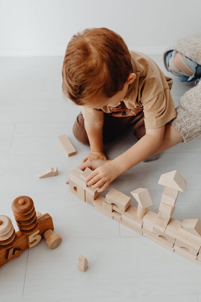 A child stacking wooden building blocks on the floor of a playroom in a creative play session.