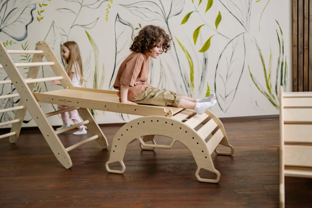 A child enjoying playtime on a wooden slide in a decorated indoor playroom.