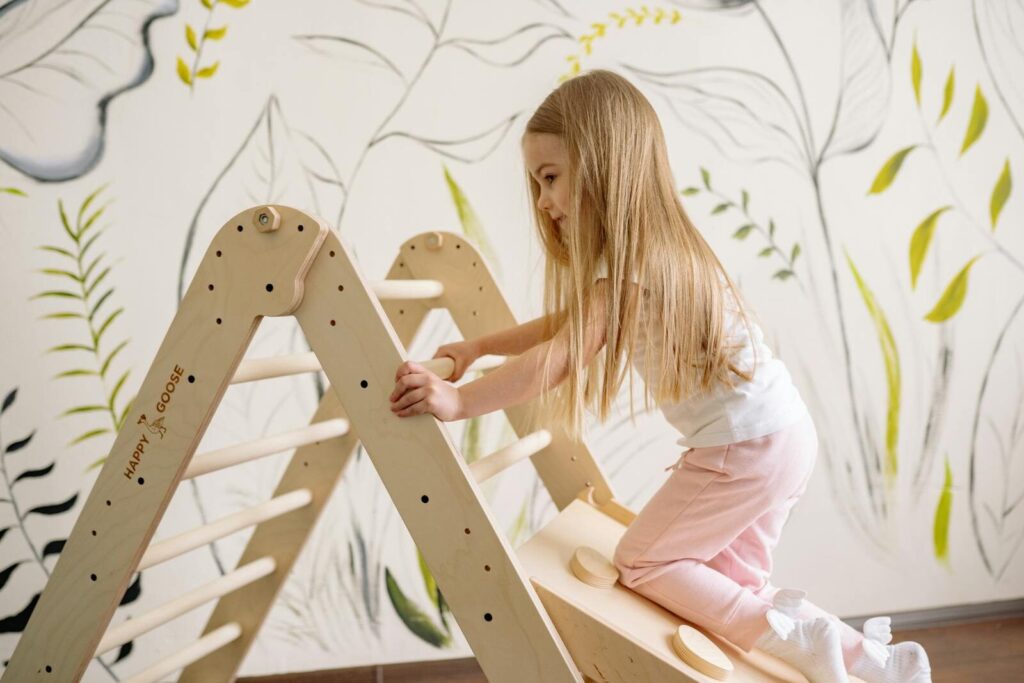 A young girl with long hair climbing an indoor wooden play ladder in a cozy room.